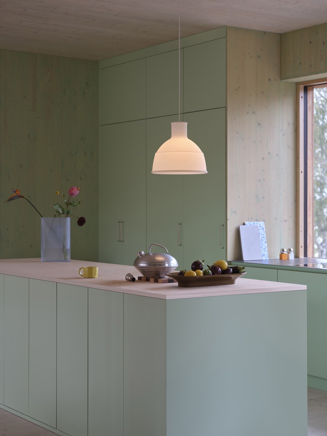 The Muuto Unfold Pendant Lamp in translucent white is paired with a light blue frosted glass Ridge Vase and a brown-green Mere Bowl. This stylish ensemble creates a harmonious, modern aesthetic, perfect for contemporary interiors seeking a blend of soft light and sculptural elegance.