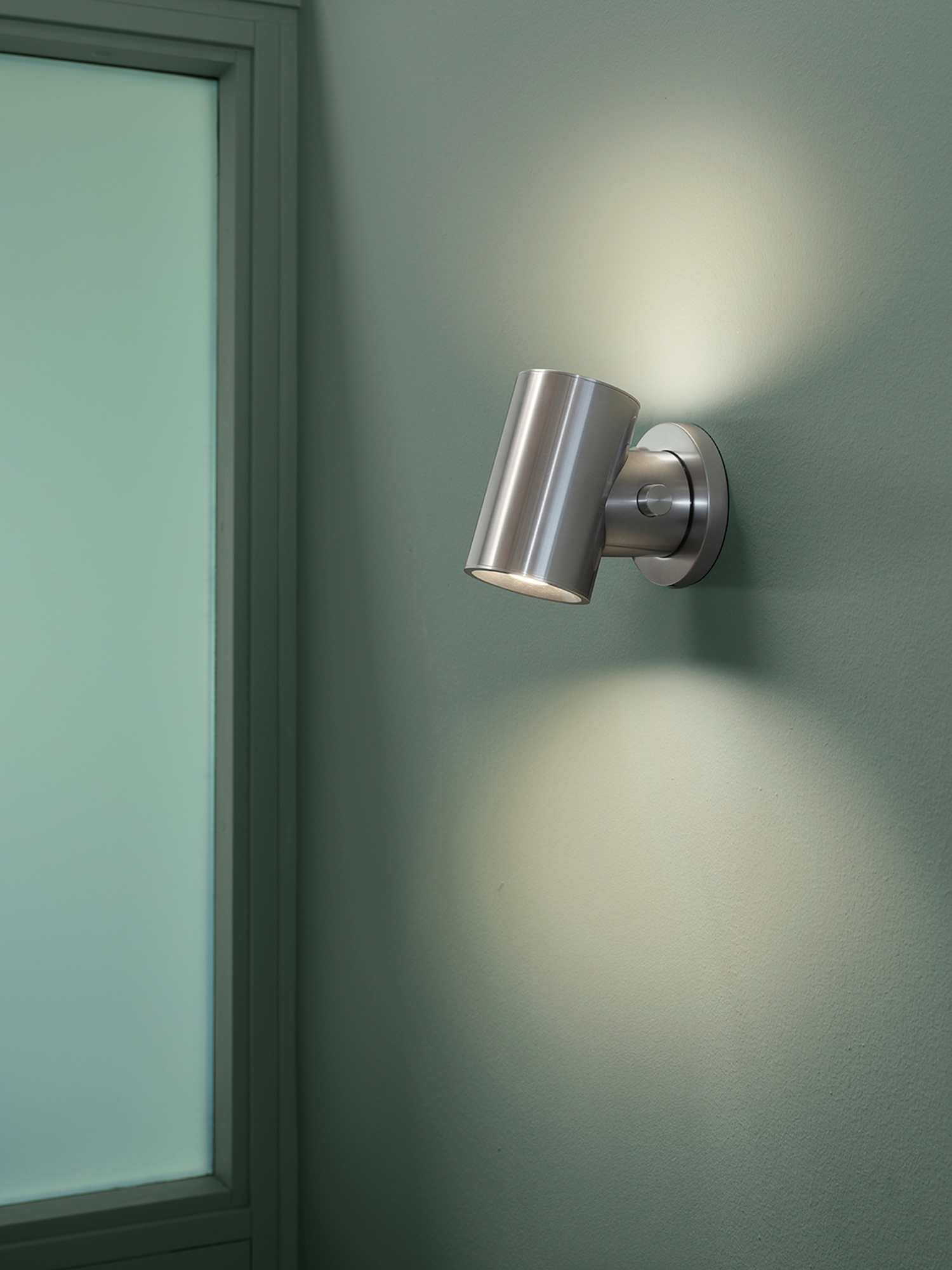 Beam Wall Lamp in polished aluminium casting a warm, comfortable light in a soft green room.
