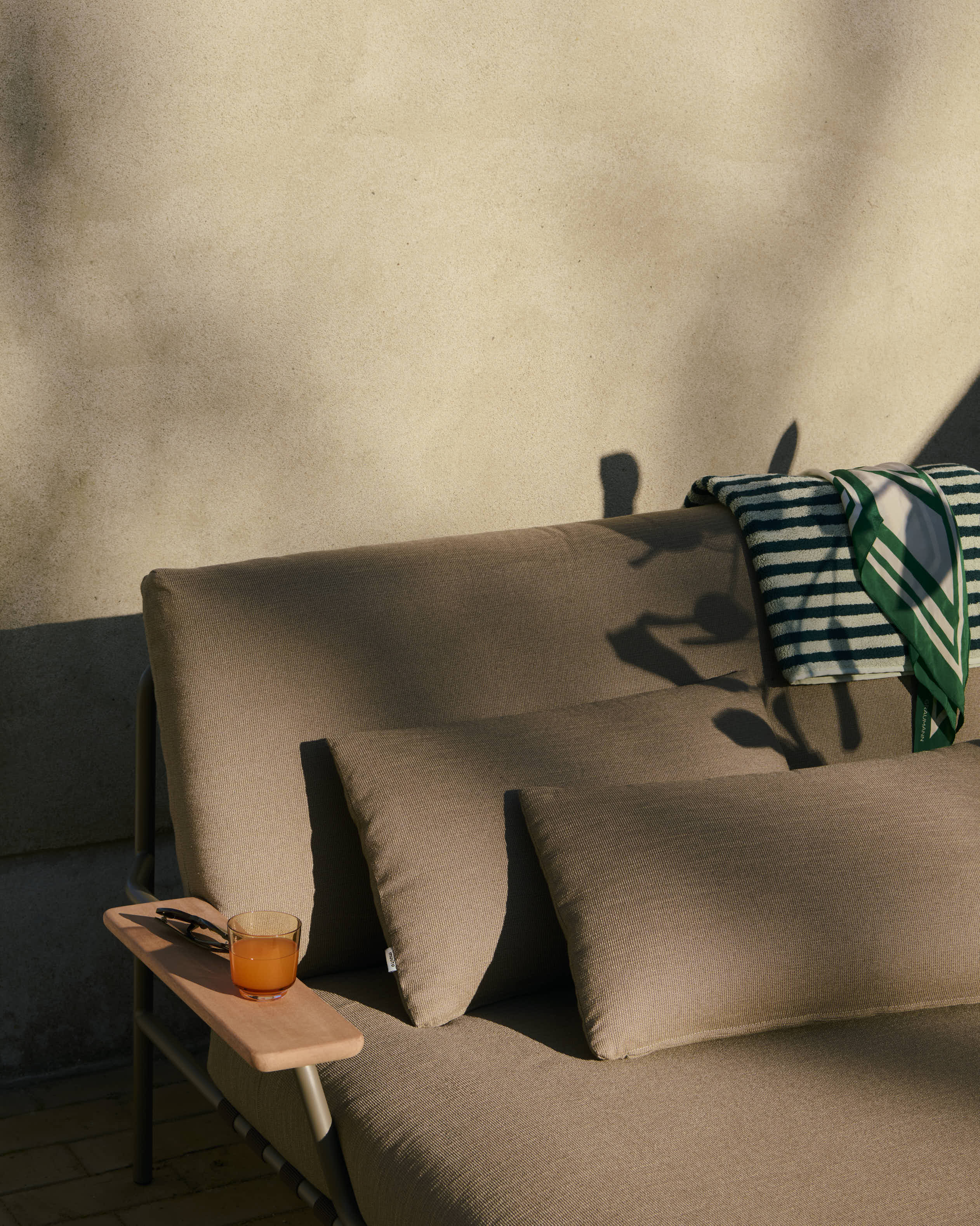 A close up of the Settle Lounge Bed with Armrest placed outdoors at sunset in a minimalistic outdoor setting. The warm glow of the setting sun highlights the sleek lines of the lounge bed, creating a cozy and inviting atmosphere perfect for relaxing or unwinding.