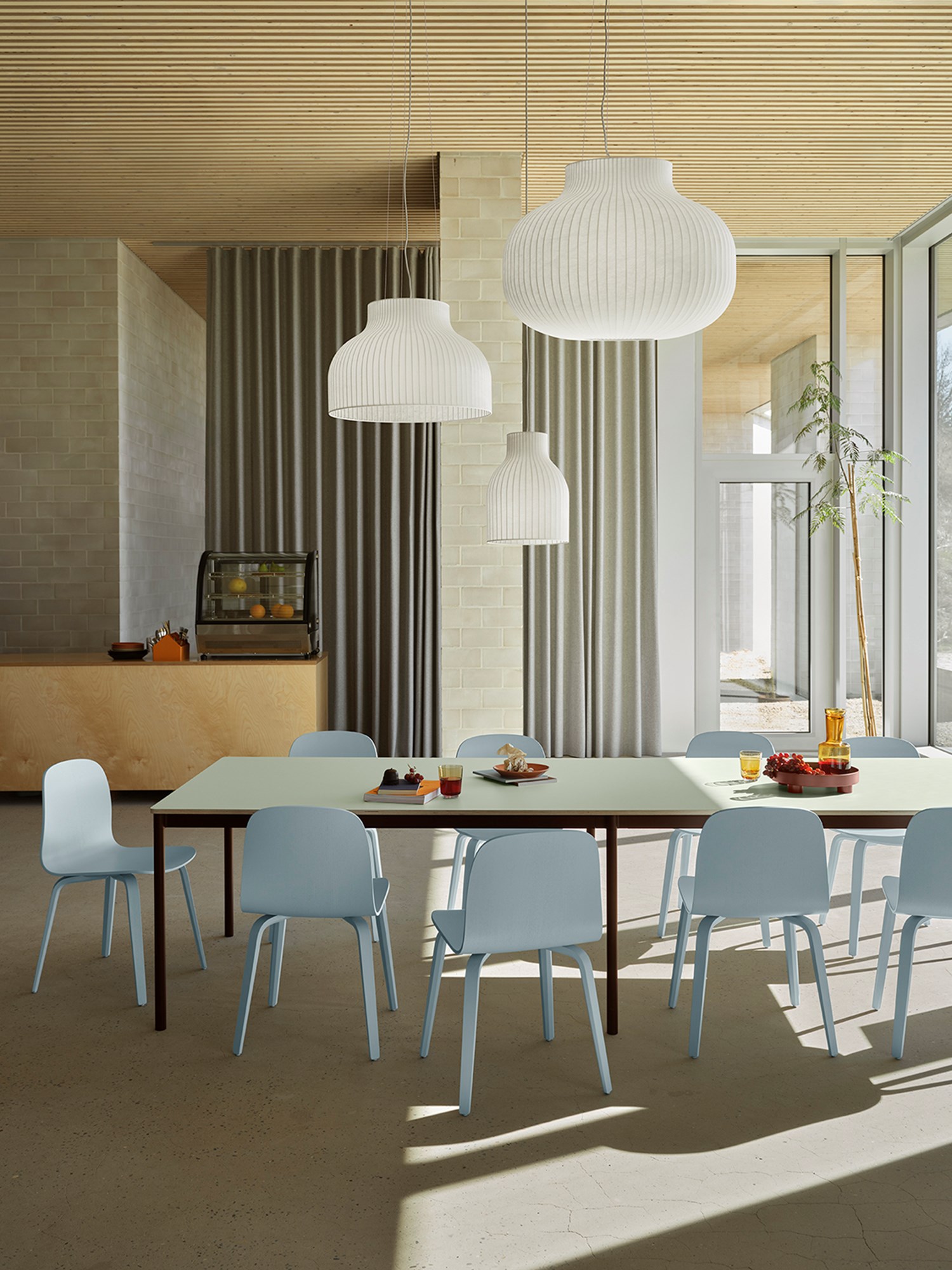 A large rectangular base table in light green, brown, and red tones, paired with light blue Visu chairs and Strand lamps. A large rectangular base table in light green, brown, and red tones, paired with light blue Visu chairs and Strand lamps.