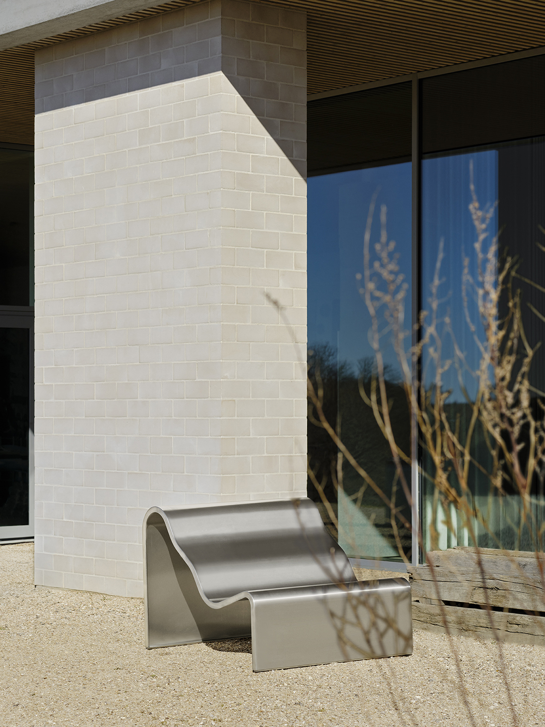 An architectural metal bench  with a wavy, sculptural design are placed outside in the sun. 