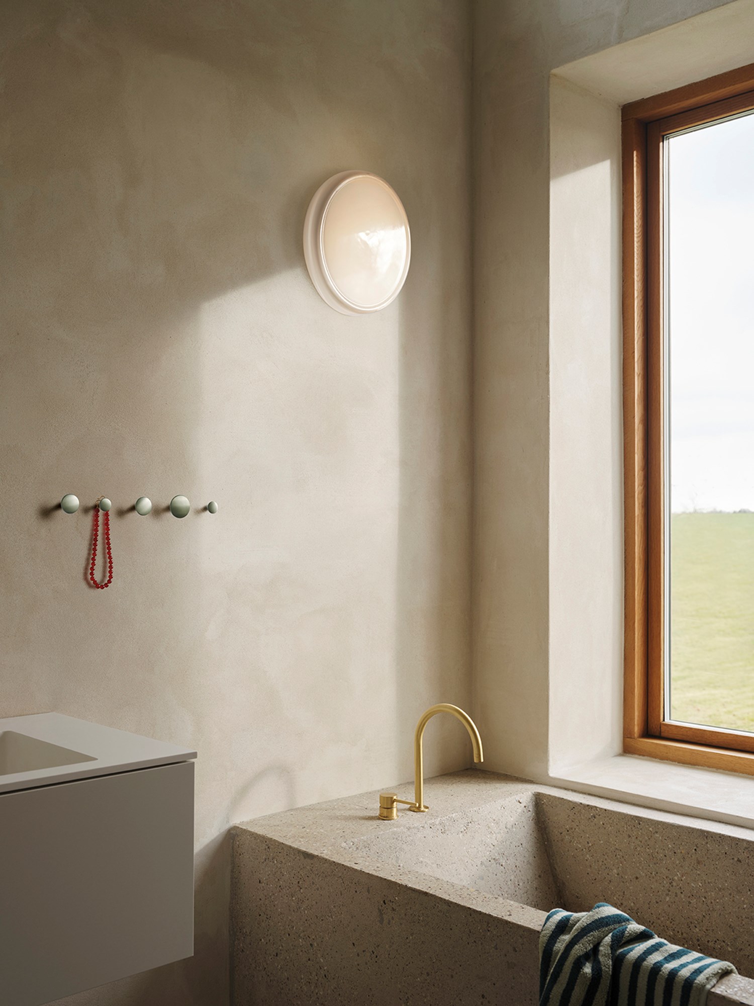 A minimalistic bathroom featuring brushed stone walls, with a round wall lamp hanging on the wall, creating a serene and modern atmosphere. A minimalistic bathroom featuring brushed stone walls, with a round wall lamp hanging on the wall, creating a serene and modern atmosphere.