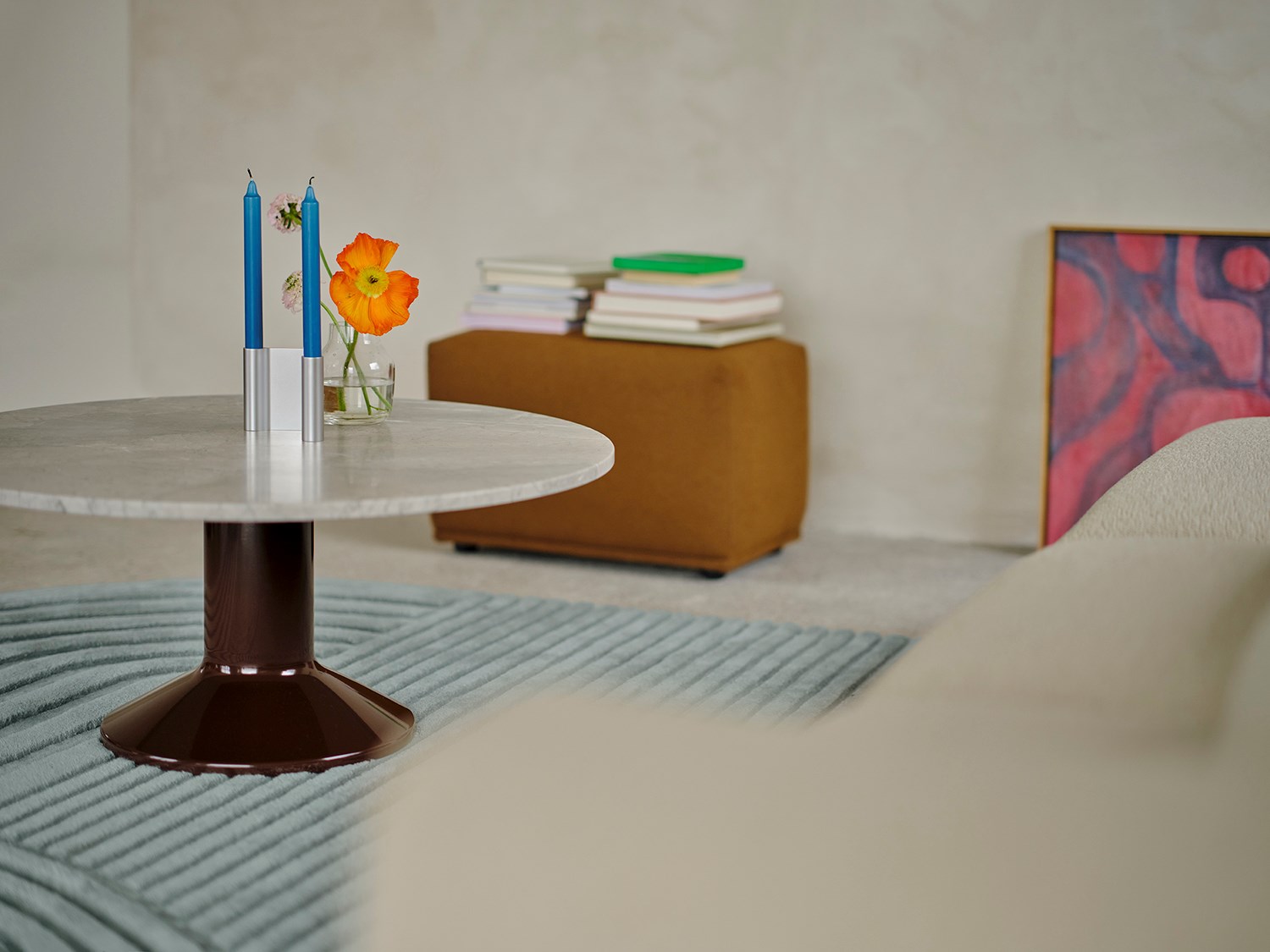 A close-up of a burgundy and marble coffee table, with a modern candle holder placed on top. A soft light blue rug is positioned underneath the table, adding warmth and creating a cozy yet contemporary setting. A close-up of a burgundy and marble coffee table, with a modern candle holder placed on top. A soft light blue rug is positioned underneath the table, adding warmth and creating a cozy yet contemporary setting.