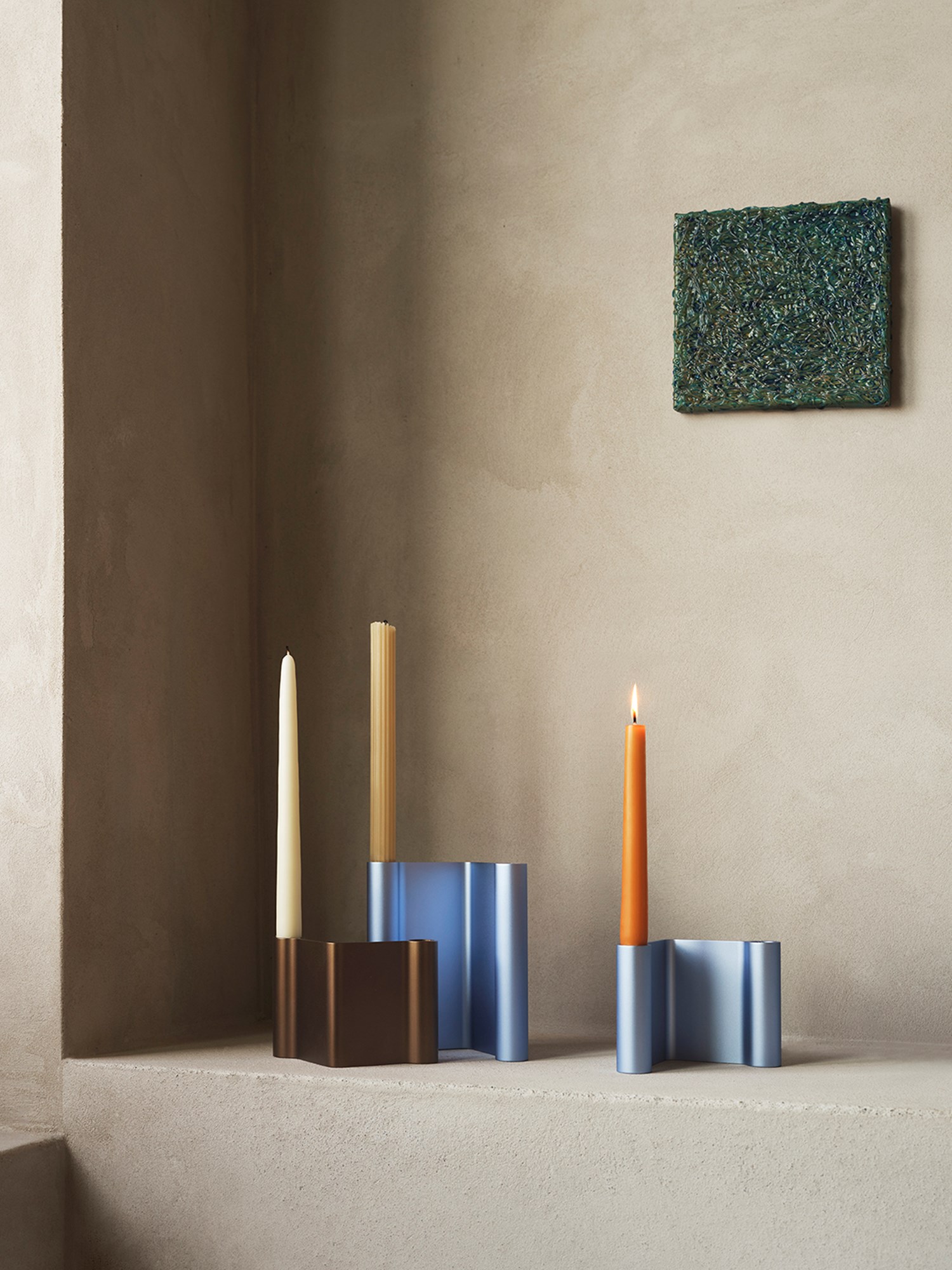 Modern candle holders in various colors are arranged on a shelf, adding vibrant accents to the grey stonewashed walls. Modern candle holders in various colors are arranged on a shelf, adding vibrant accents to the grey stonewashed walls.