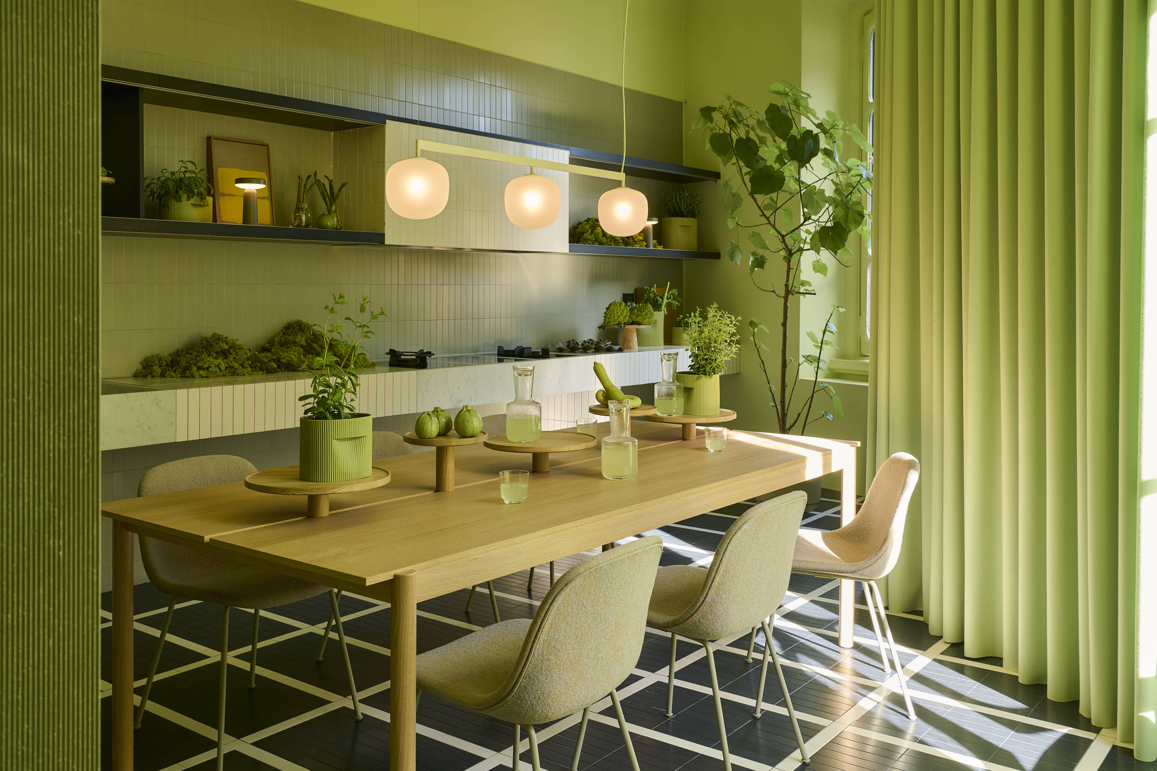A light green room with rays of sunlight. The room is styled with a wooden dining table, accompanied by soft dining chairs. Vases and glasses are placed on the table. A modern pendant lamp hangs from the ceiling.