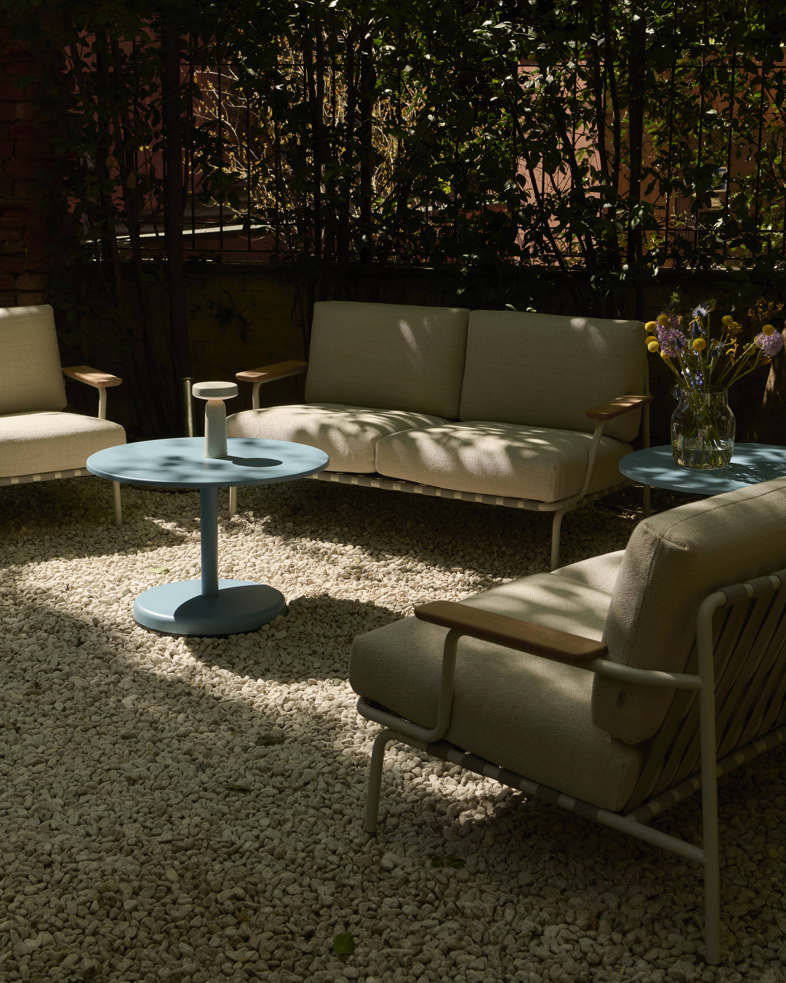 In a cozy courtyard, some outdoor furniture is placed in the shade. A light blue metal coffee table is positioned in the middle of the setting.