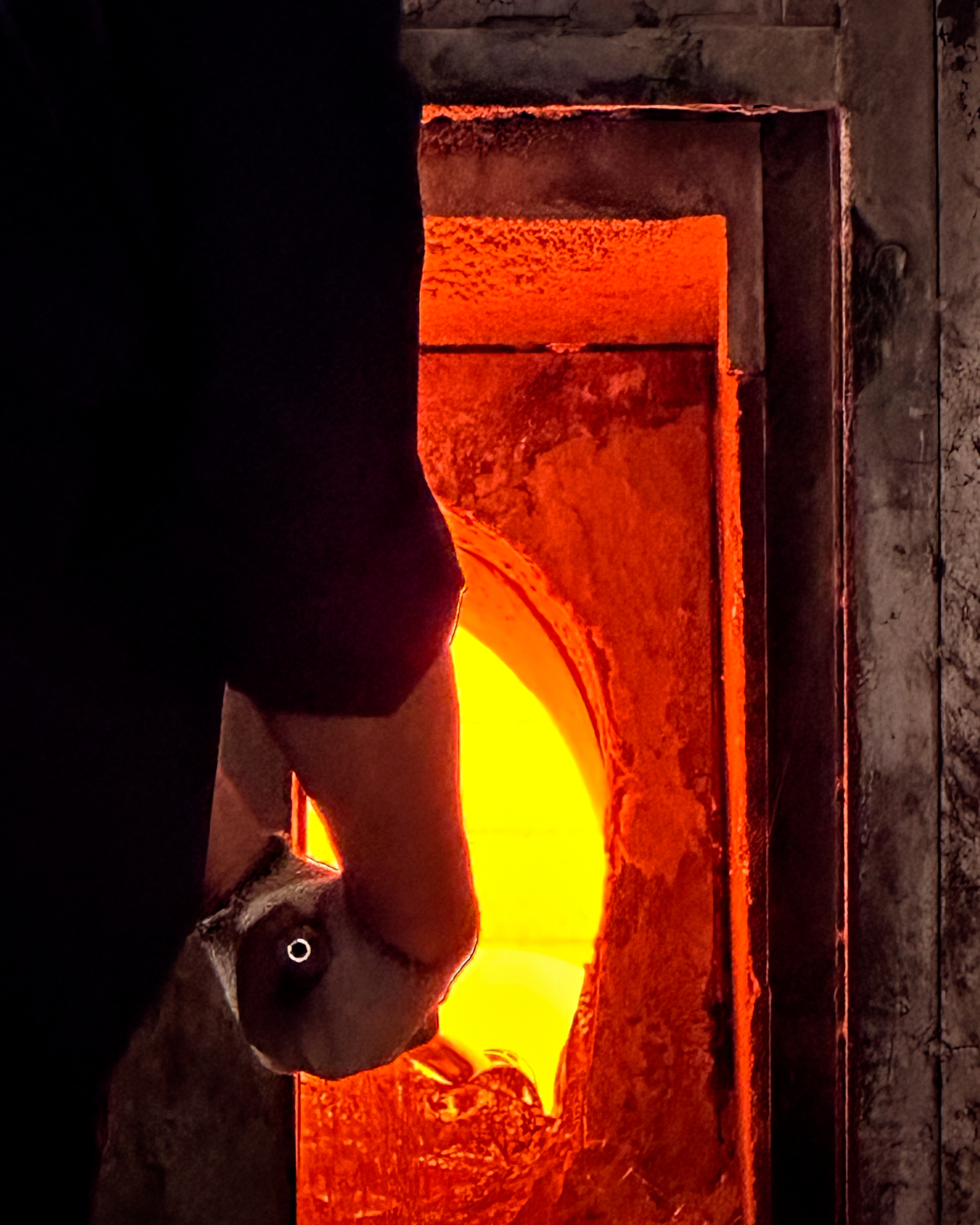 A close-up shot of a person’s hand holding a tool as they work near a furnace.