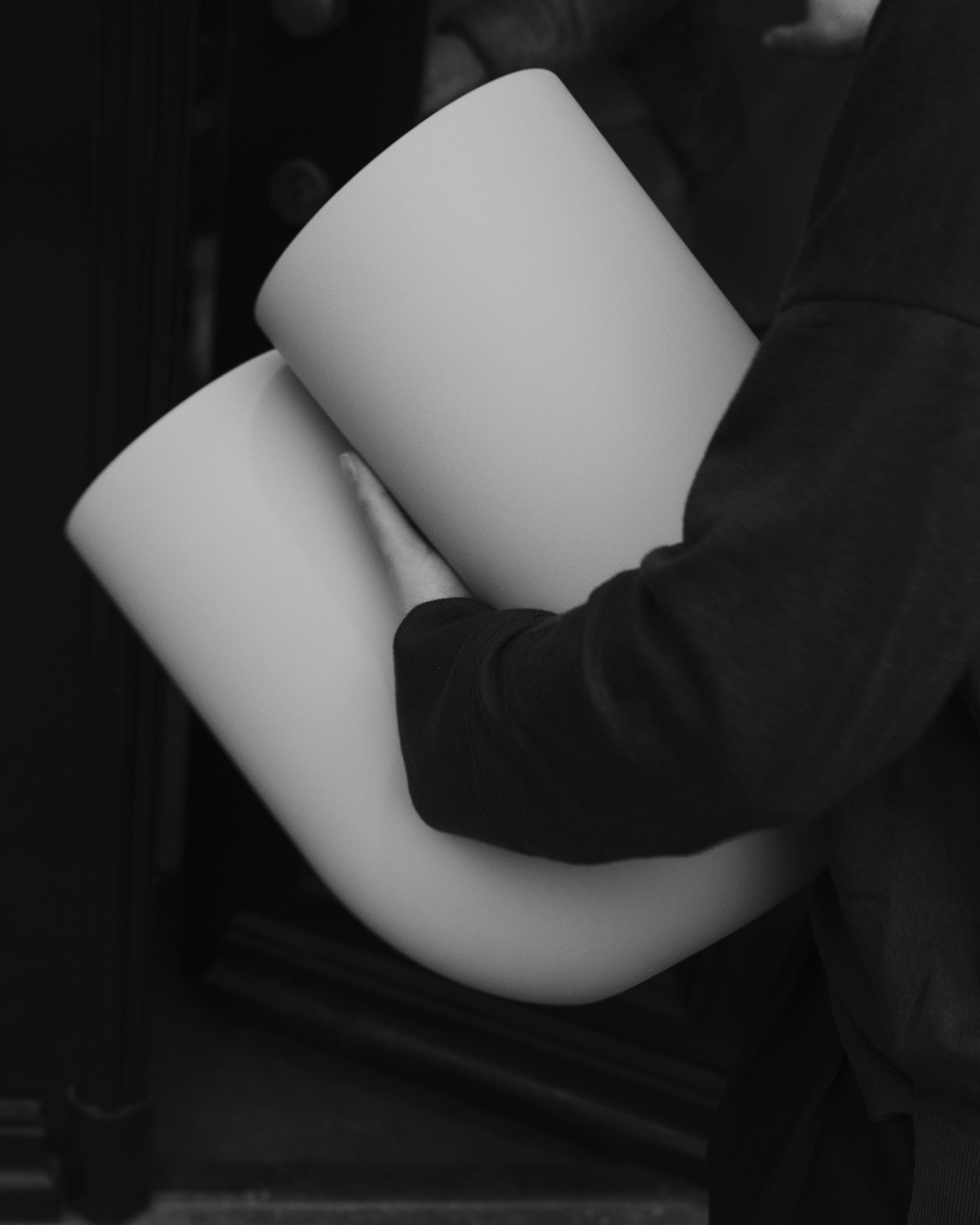In a black-and-white close-up, Rachel holds a Kink Vase close to their torso. 

