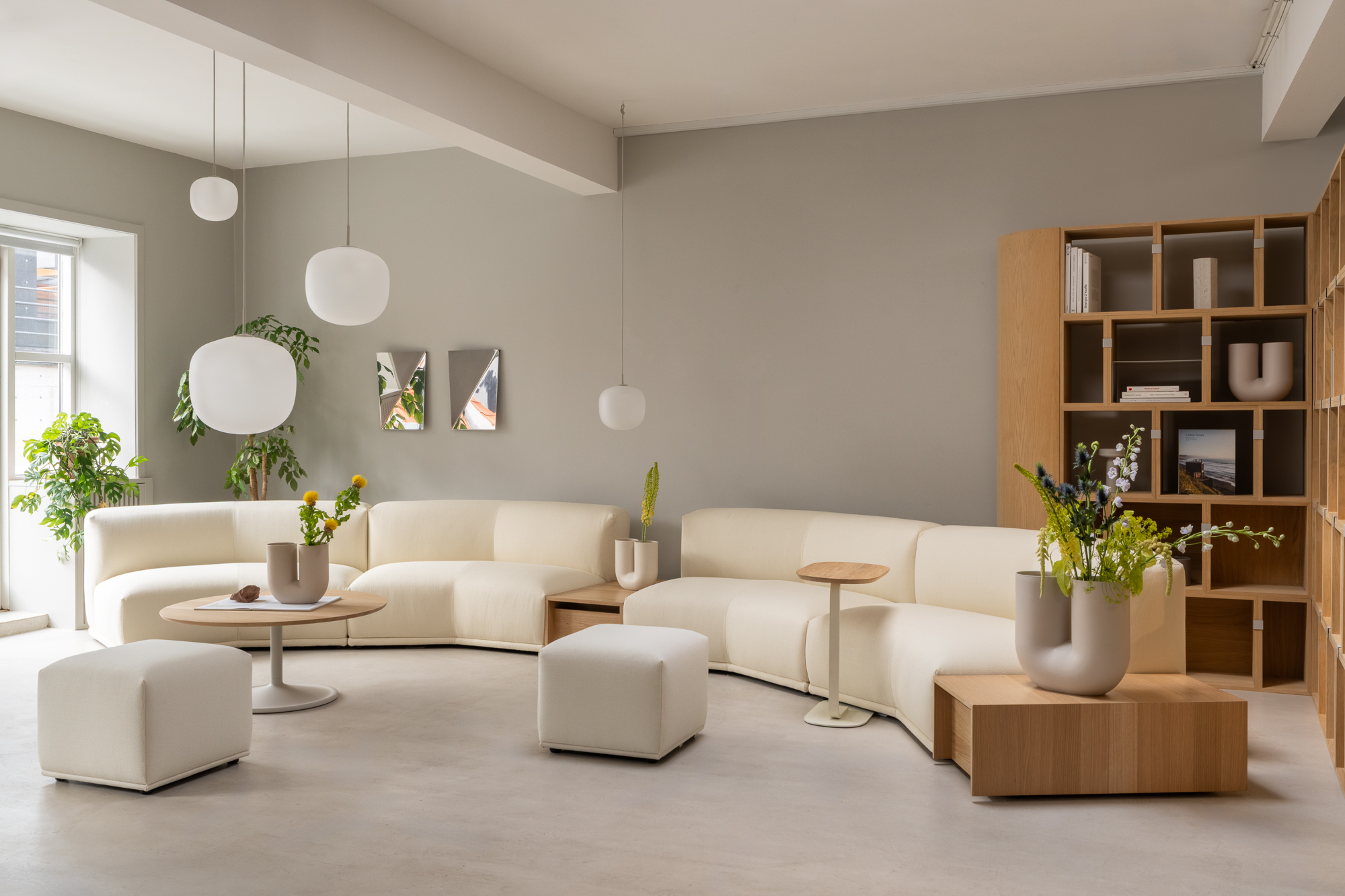 A minimalistic room with white Connect sofas and a  storage system in wood. Lamps in different height are hanging from the ceiling and green plants in sculptural vases are creating a  nice lounge area.