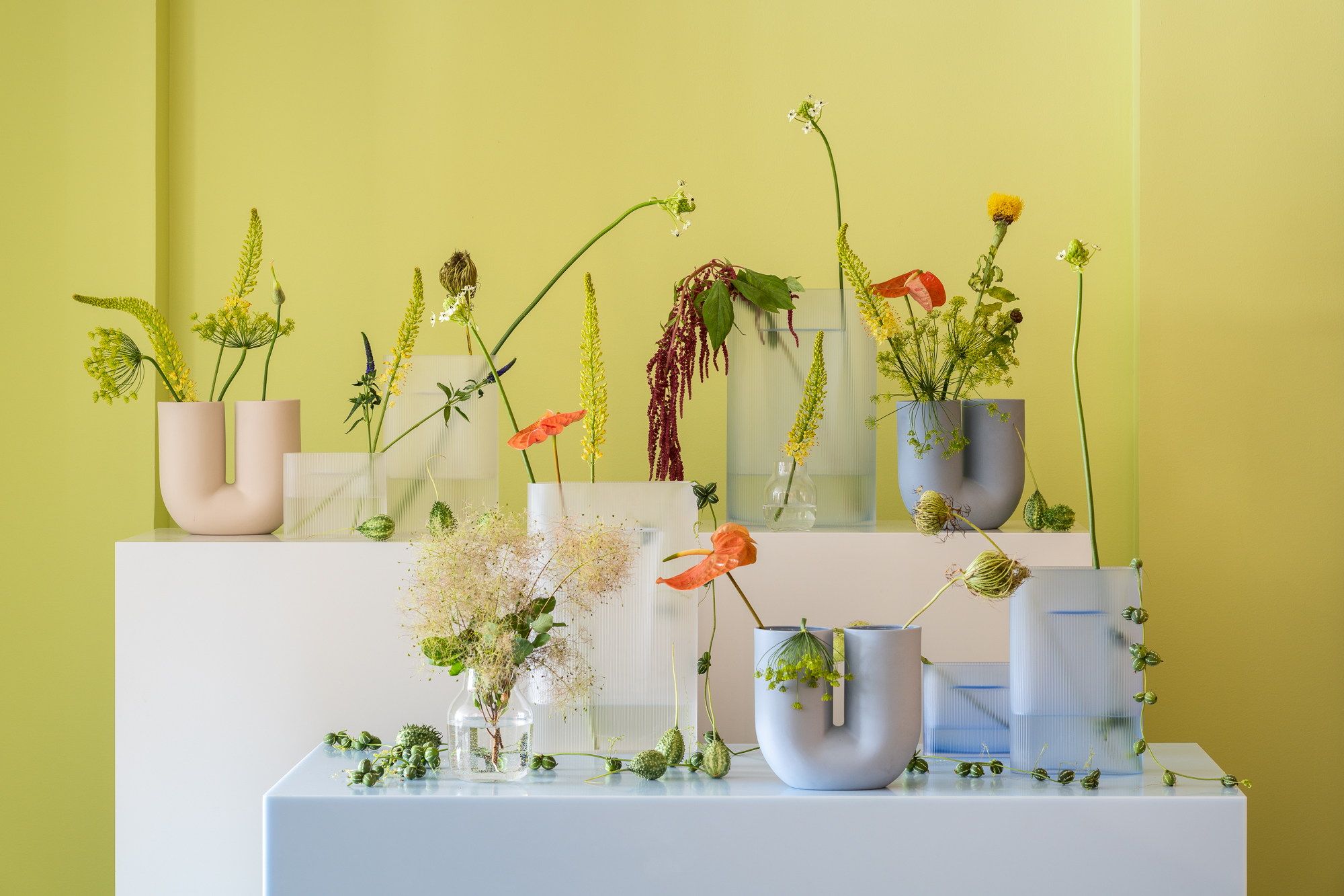 Vases in varying colors, materials, and designs are arranged in an artistic composition, each adorned with decorative flowers to create a modern and visually engaging setup.