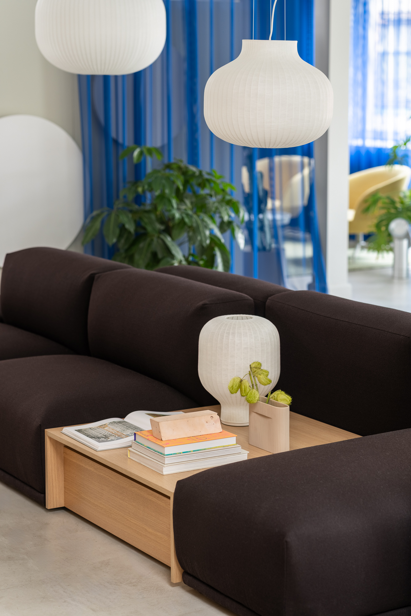 Two Strand Pendant Lamps hang above a dark modular sofa, casting soft light over the seating area. A wooden sofa table is placed at the center of the arrangement, adding warmth and functionality to the modern setup.