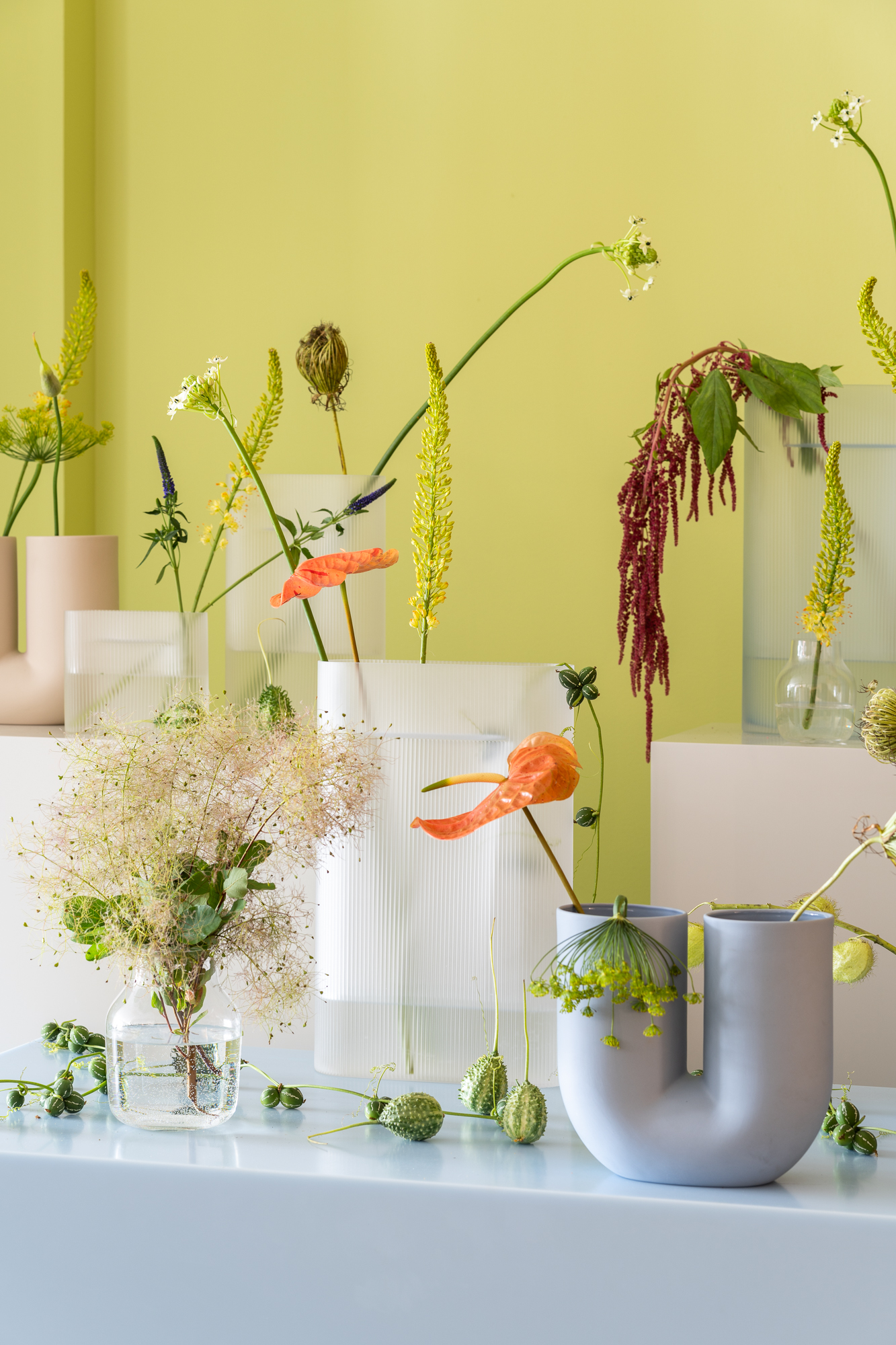 Vases in varying colors, materials, and designs are arranged in an artistic composition, each adorned with decorative flowers to create a modern and visually engaging setup.