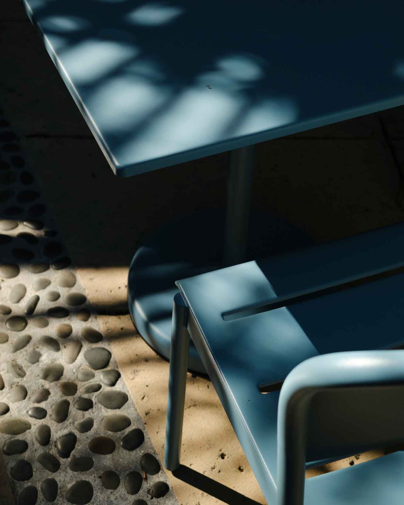 Close up of a pale blue outdoor café table and chair placed in the shadow.